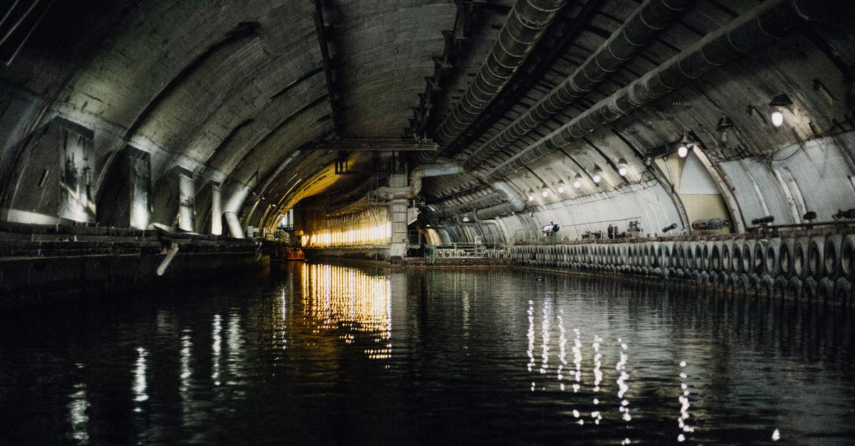 Dark and atmospheric underground canal tunnel with water reflections and industrial architecture.